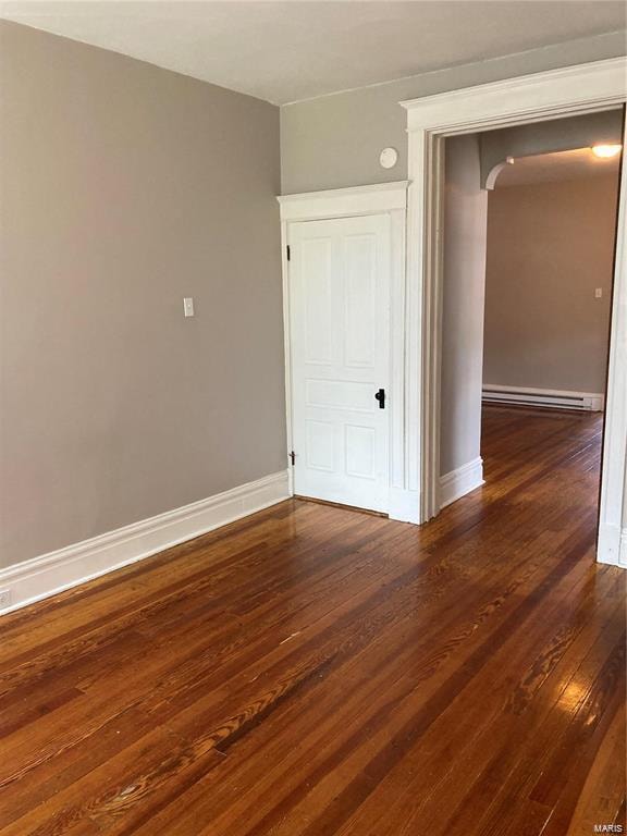 empty room featuring dark wood-type flooring and a baseboard heating unit