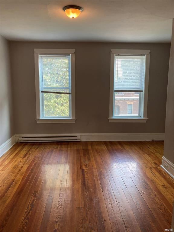 empty room with dark hardwood / wood-style floors and a baseboard radiator