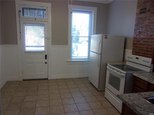 kitchen with white appliances, stone countertops, a wealth of natural light, and light tile patterned flooring