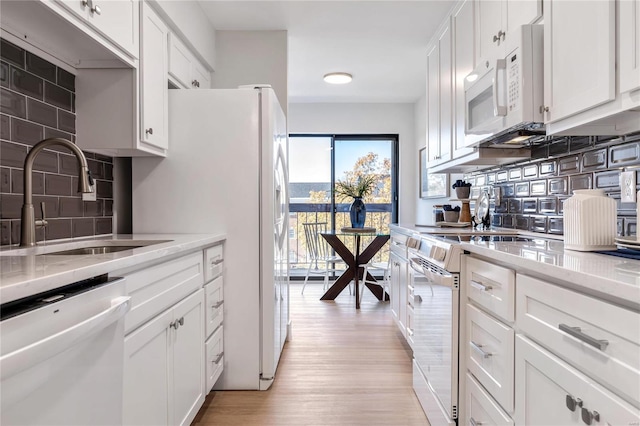 kitchen featuring white appliances, backsplash, sink, light wood-type flooring, and white cabinetry