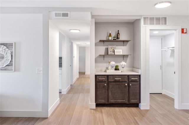 bar with dark brown cabinetry and light wood-type flooring