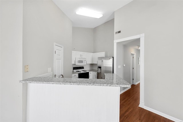 kitchen with kitchen peninsula, light stone countertops, white appliances, white cabinets, and dark hardwood / wood-style floors