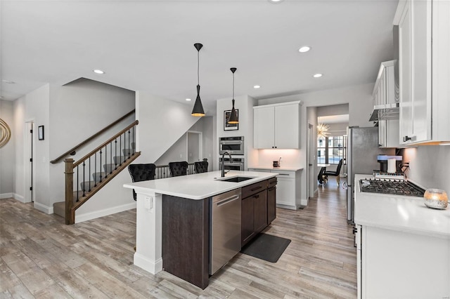 kitchen featuring stainless steel appliances, sink, decorative light fixtures, white cabinetry, and an island with sink