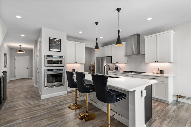 kitchen featuring appliances with stainless steel finishes, pendant lighting, an island with sink, and wall chimney exhaust hood