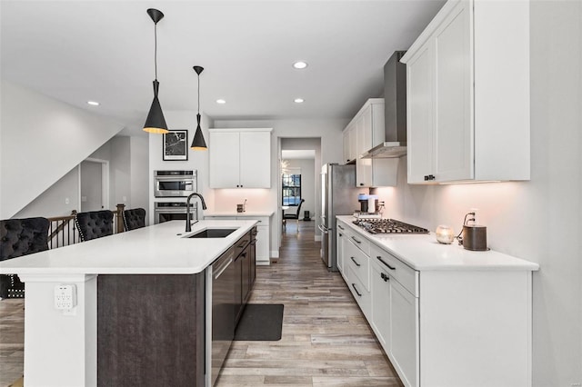 kitchen featuring sink, white cabinets, wall chimney exhaust hood, pendant lighting, and a kitchen island with sink