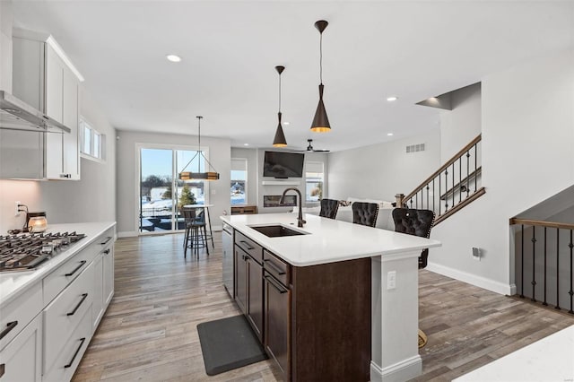 kitchen featuring sink, white cabinets, an island with sink, stainless steel gas stovetop, and wall chimney range hood