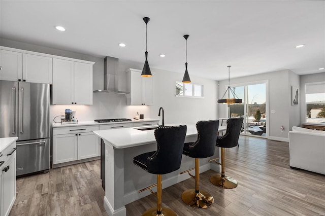 kitchen with white cabinetry, wall chimney exhaust hood, a kitchen breakfast bar, an island with sink, and high end fridge