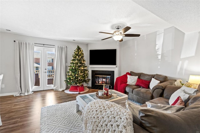 living room featuring french doors, a textured ceiling, ceiling fan, hardwood / wood-style flooring, and a tiled fireplace