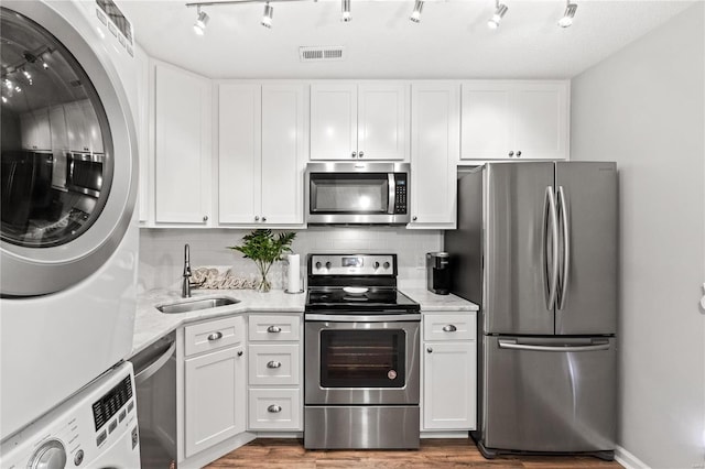 kitchen featuring backsplash, white cabinets, sink, stacked washing maching and dryer, and appliances with stainless steel finishes