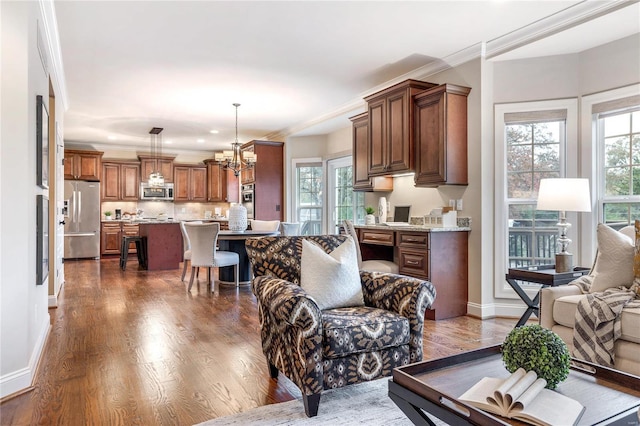 living room with dark wood-type flooring, an inviting chandelier, a wealth of natural light, and ornamental molding