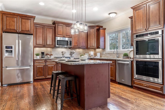 kitchen featuring a center island, hanging light fixtures, tasteful backsplash, light stone counters, and appliances with stainless steel finishes