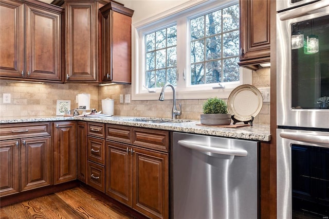 kitchen with dark wood-type flooring, sink, tasteful backsplash, light stone counters, and stainless steel appliances