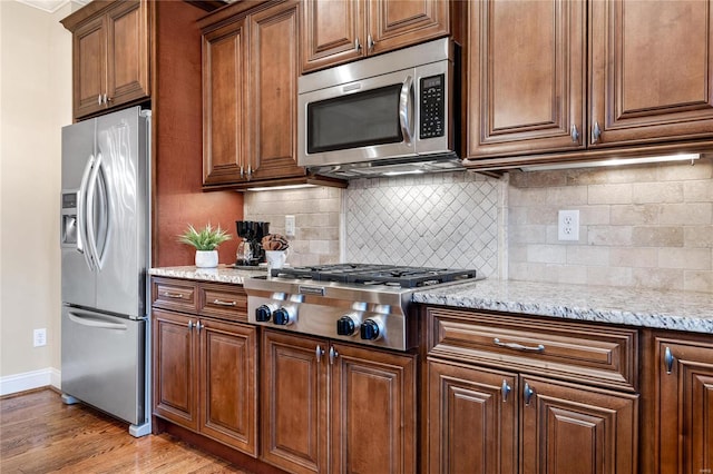 kitchen featuring light stone countertops, light wood-type flooring, stainless steel appliances, and tasteful backsplash