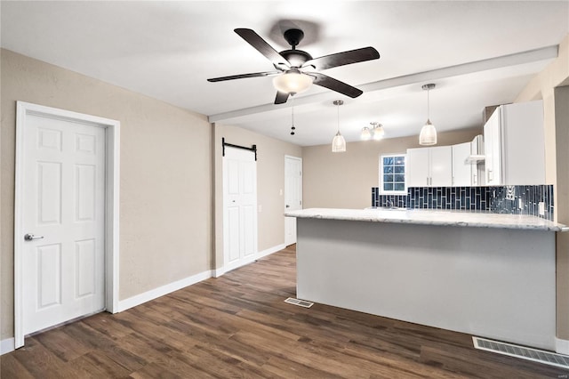 kitchen featuring dark wood-type flooring, decorative backsplash, a barn door, decorative light fixtures, and white cabinetry