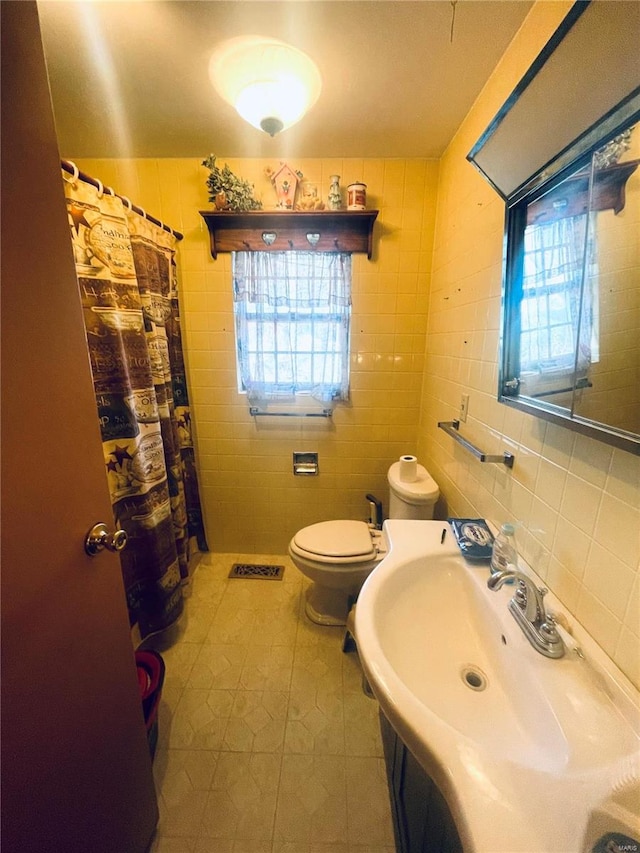 bathroom with toilet, tile patterned flooring, tile walls, and sink