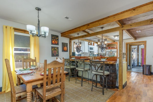 dining room with beam ceiling, light wood-type flooring, and an inviting chandelier