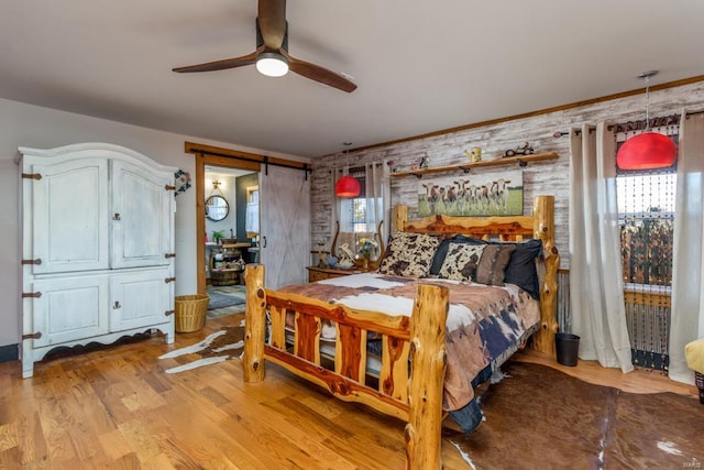 bedroom featuring ceiling fan, a barn door, light hardwood / wood-style flooring, and multiple windows