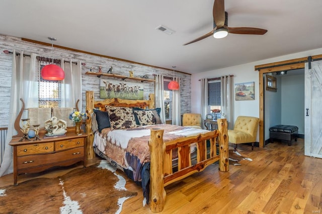 bedroom with hardwood / wood-style flooring, ceiling fan, and a barn door