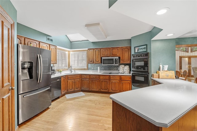 kitchen featuring sink, decorative backsplash, light wood-type flooring, and black appliances