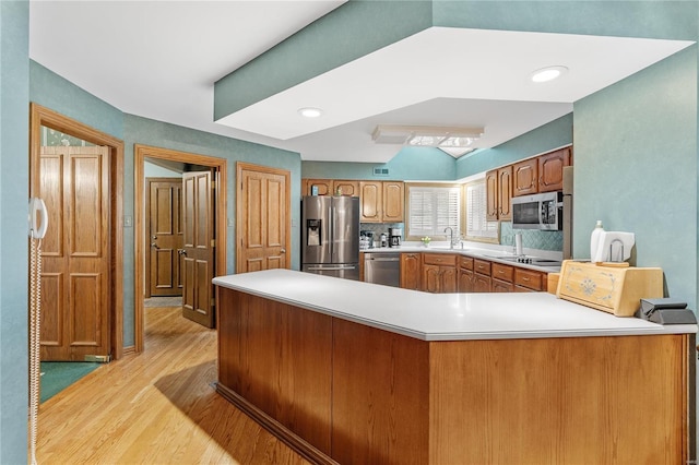 kitchen featuring kitchen peninsula, appliances with stainless steel finishes, light wood-type flooring, backsplash, and sink