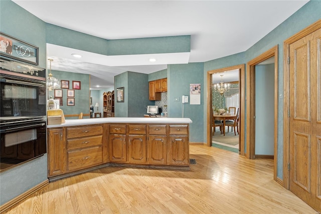 kitchen with a chandelier, kitchen peninsula, black double oven, and light hardwood / wood-style flooring