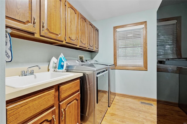 washroom with cabinets, washing machine and dryer, light wood-type flooring, and sink