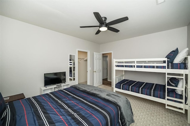 carpeted bedroom featuring a walk in closet and ceiling fan