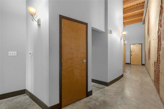 hall featuring concrete flooring, a towering ceiling, and baseboards