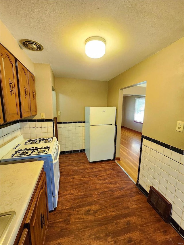 kitchen featuring a textured ceiling, white appliances, tile walls, and dark wood-type flooring