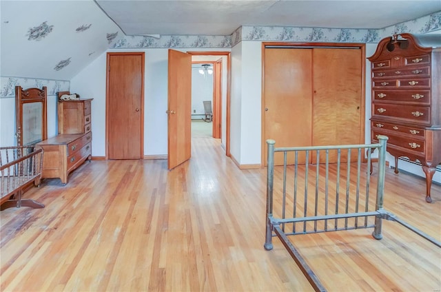 bedroom with a baseboard heating unit, a closet, lofted ceiling, and light wood-type flooring