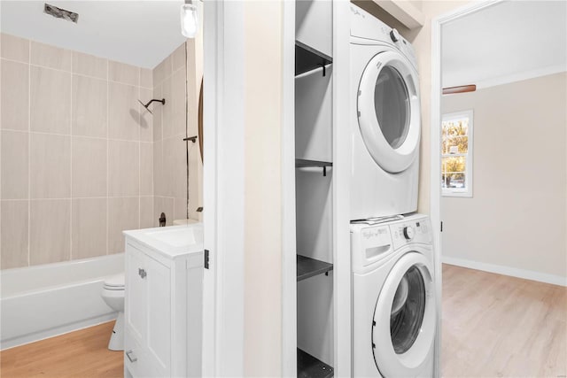 laundry area with light wood-type flooring, stacked washer / dryer, and ornamental molding