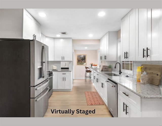 kitchen with sink, tasteful backsplash, light hardwood / wood-style floors, white cabinetry, and stainless steel appliances