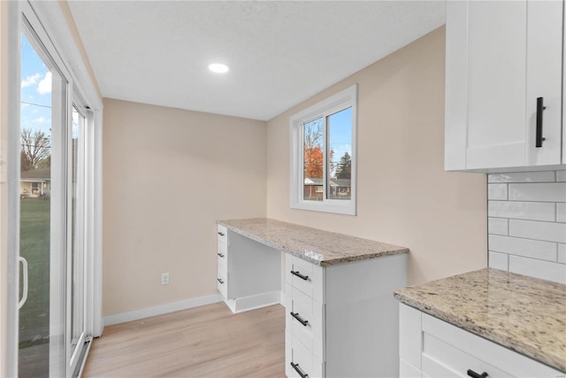 kitchen with white cabinets, decorative backsplash, a textured ceiling, light hardwood / wood-style floors, and light stone counters