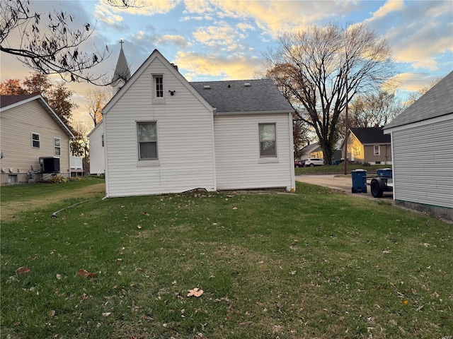 back house at dusk with a lawn and central AC