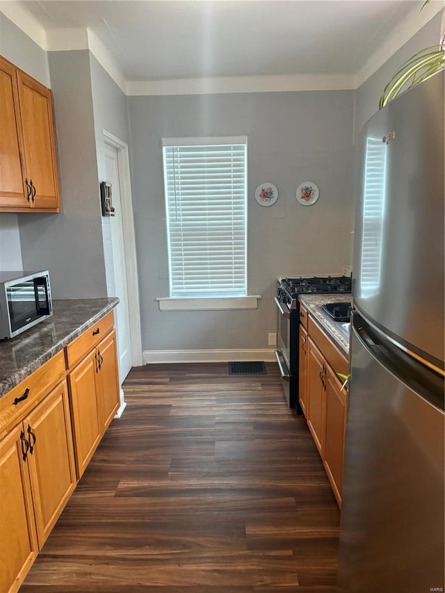 kitchen featuring dark stone countertops, dark hardwood / wood-style flooring, stainless steel appliances, and ornamental molding