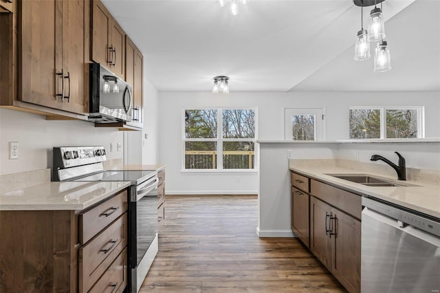 kitchen featuring decorative light fixtures, stainless steel appliances, a sink, wood finished floors, and baseboards