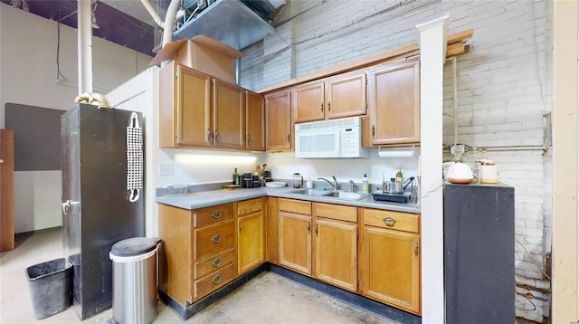 kitchen featuring stainless steel fridge, sink, and brick wall