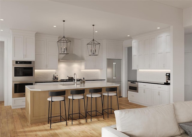 kitchen with appliances with stainless steel finishes, light wood-type flooring, a kitchen island with sink, white cabinetry, and hanging light fixtures