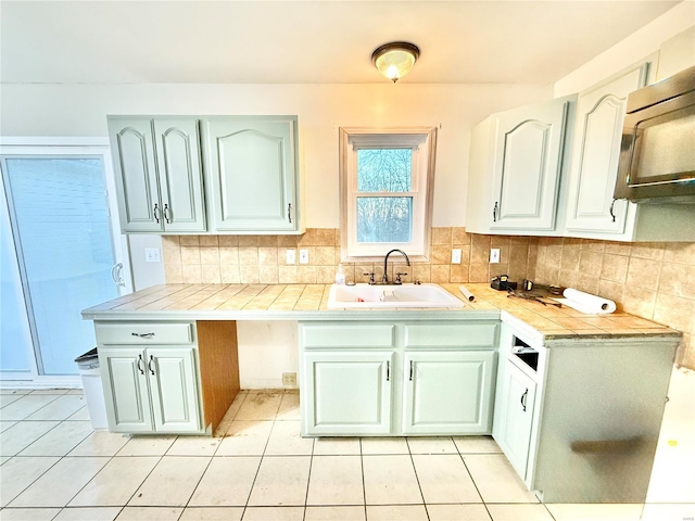 kitchen with kitchen peninsula, light tile patterned floors, backsplash, and sink