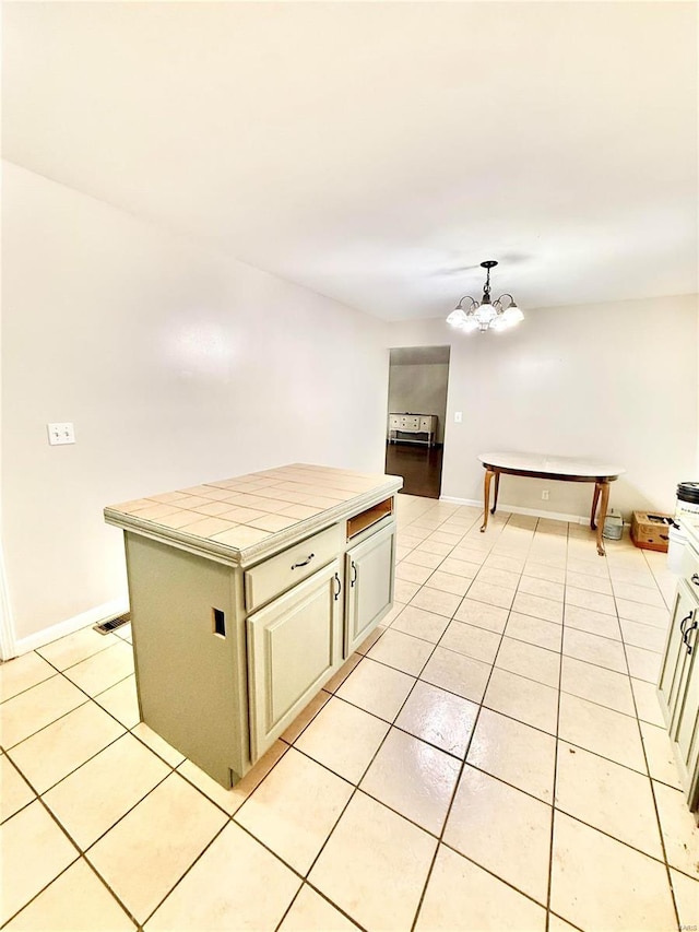 kitchen with tile counters, a kitchen island, pendant lighting, a chandelier, and light tile patterned floors