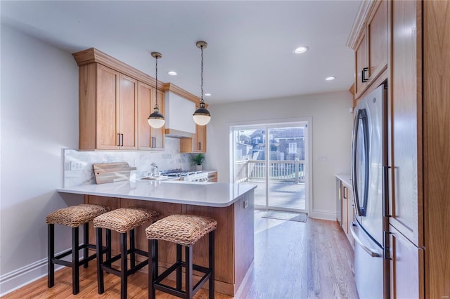 kitchen featuring hanging light fixtures, kitchen peninsula, light hardwood / wood-style flooring, and stainless steel appliances