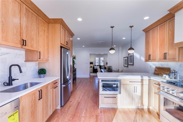 kitchen with appliances with stainless steel finishes, tasteful backsplash, sink, pendant lighting, and light hardwood / wood-style flooring