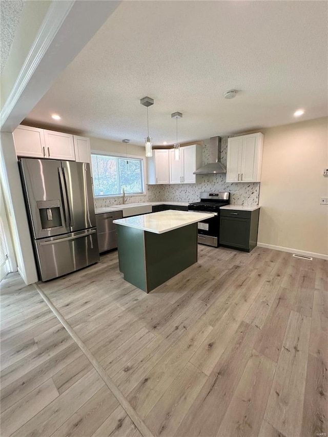 kitchen featuring pendant lighting, a center island, wall chimney exhaust hood, white cabinetry, and stainless steel appliances