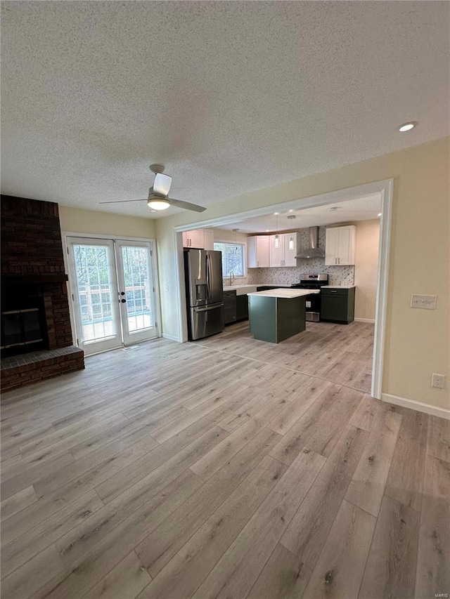 kitchen featuring backsplash, stainless steel appliances, wall chimney range hood, light hardwood / wood-style floors, and a kitchen island