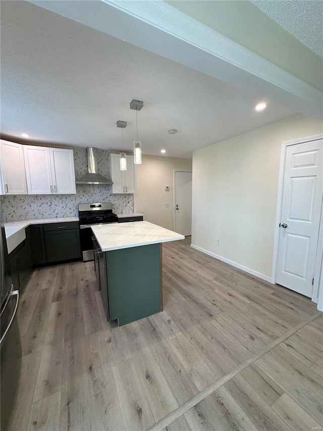 kitchen featuring wall chimney exhaust hood, stainless steel range, pendant lighting, light hardwood / wood-style floors, and white cabinetry