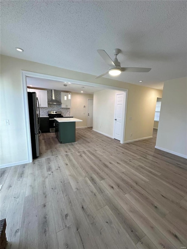 unfurnished living room with a textured ceiling, light wood-type flooring, and ceiling fan