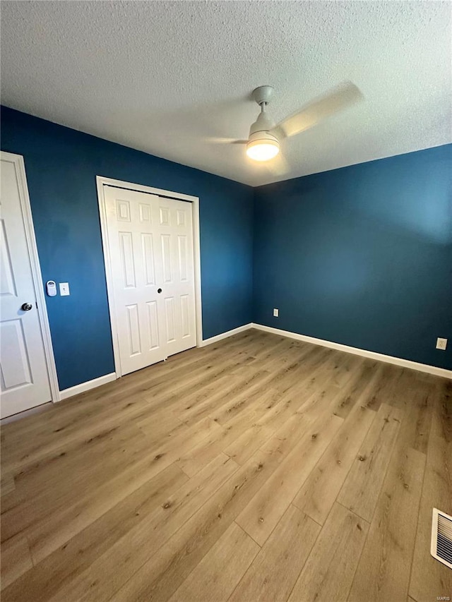 unfurnished bedroom featuring ceiling fan, light wood-type flooring, a textured ceiling, and a closet