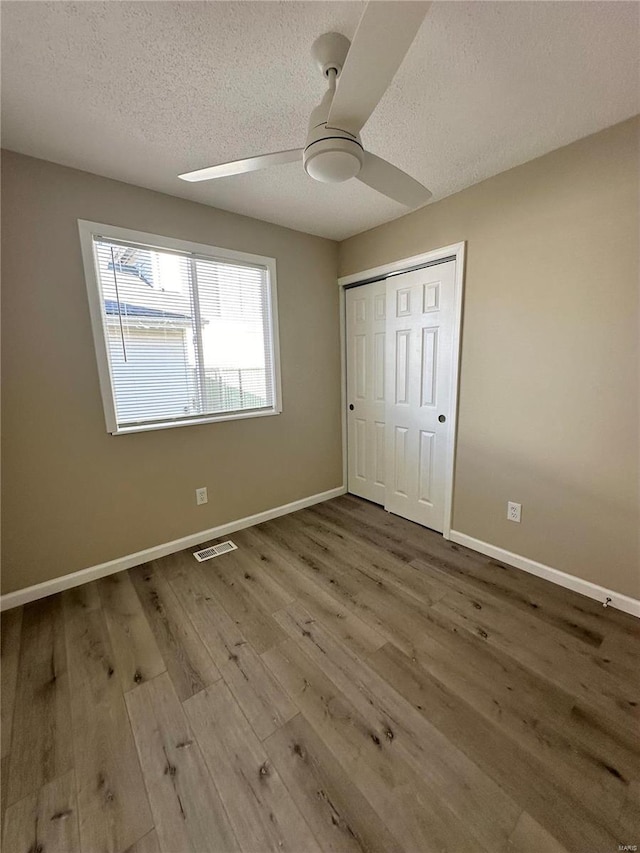 unfurnished bedroom featuring ceiling fan, a closet, wood-type flooring, and a textured ceiling