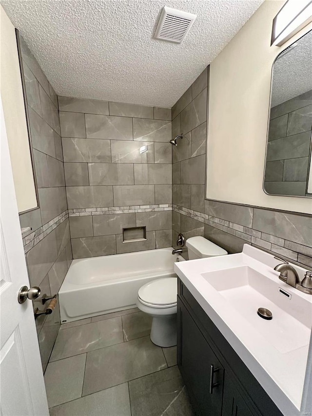 full bathroom with tile patterned floors, a textured ceiling, tiled shower / bath combo, tile walls, and toilet