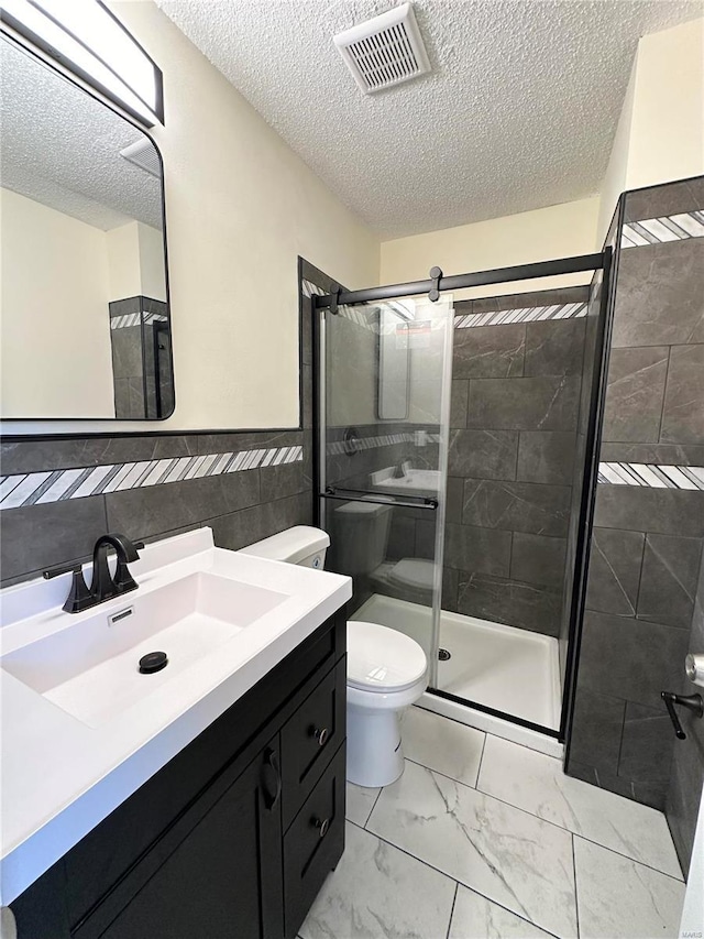 bathroom with a textured ceiling, toilet, a shower with door, vanity, and tile walls